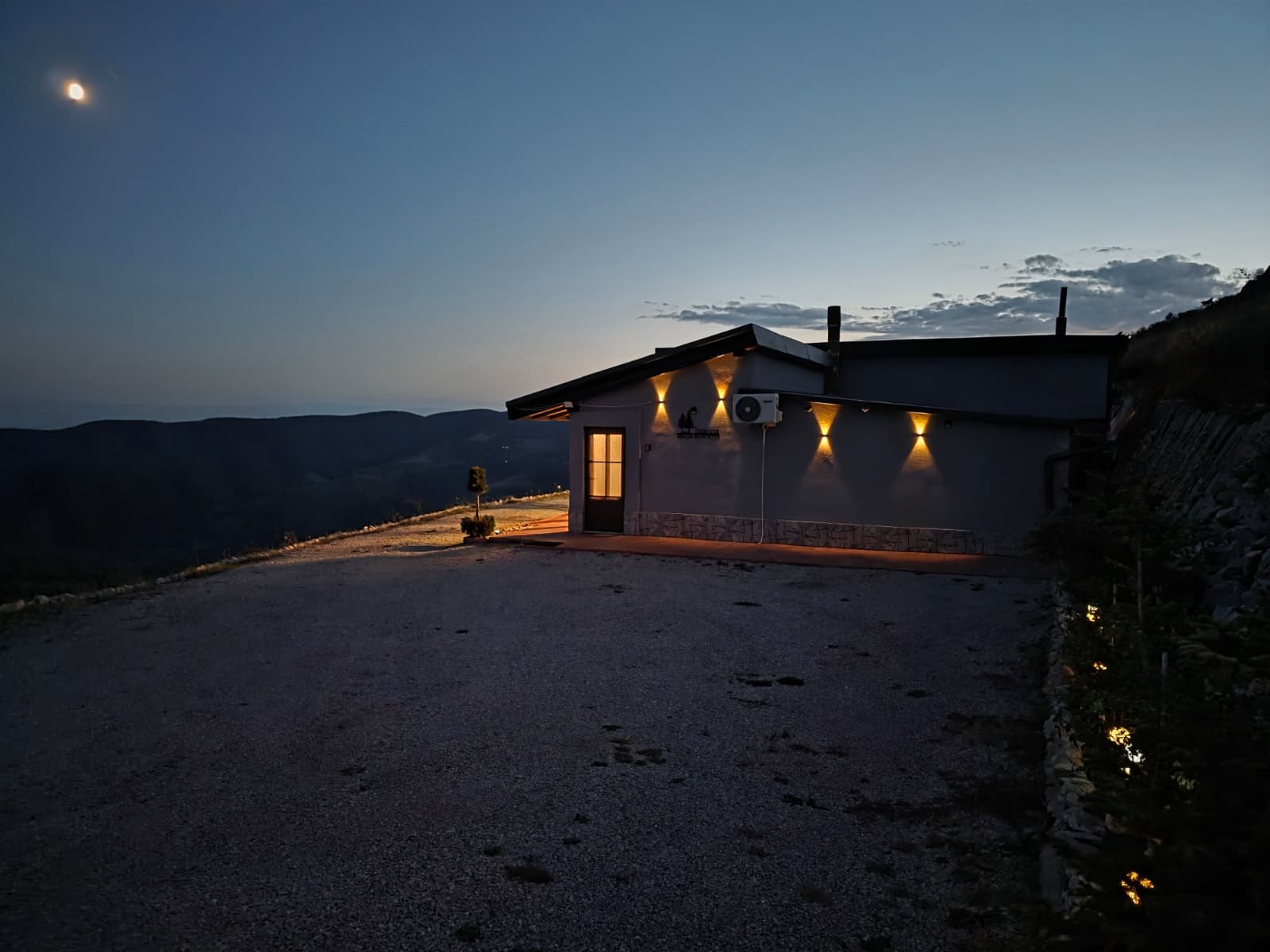 Casa iluminată seara, cu luna deasupra crestelor și valea cufundată în întuneric